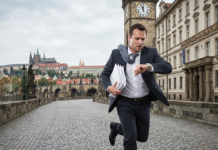 Fisco ceco 2026: le scadenze e i nuovi importi per non farsi trovare impreparati Un uomo in abito elegante corre trafelato sul Ponte Carlo a Praga verso l'ufficio delle tasse, tenendo dei documenti in mano e guardando l'orologio, con il castello di Praga sullo sfondo.