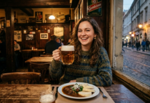 Mangiare a Praga senza farsi pelare: manuale di sopravvivenza gastronomica (Edizione 2026) Una giovane donna ceca sorridente seduta in una taverna tradizionale di Praga (hospoda), con un boccale di birra artigianale in mano e un piatto di gulasch con canederli davanti a sé. Sullo sfondo, una finestra mostra una tipica via acciottolata del quartiere Žižkov al crepuscolo.